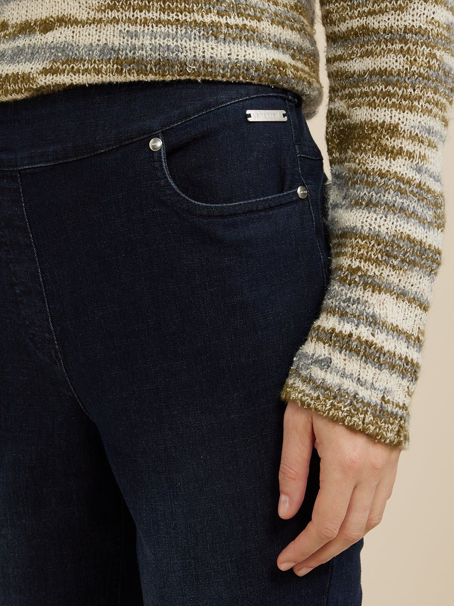 Person wearing a striped sweater and dark denim pull on jeans with a beige background