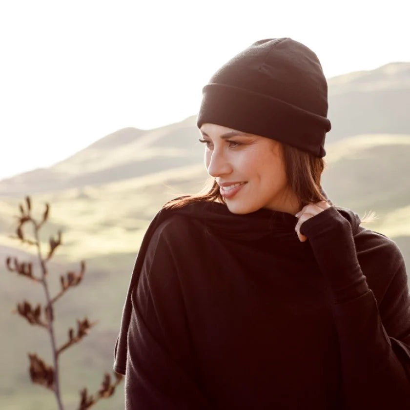 Woman wearing a black merino wool beanie poncho and gloves against a mountainous landscape