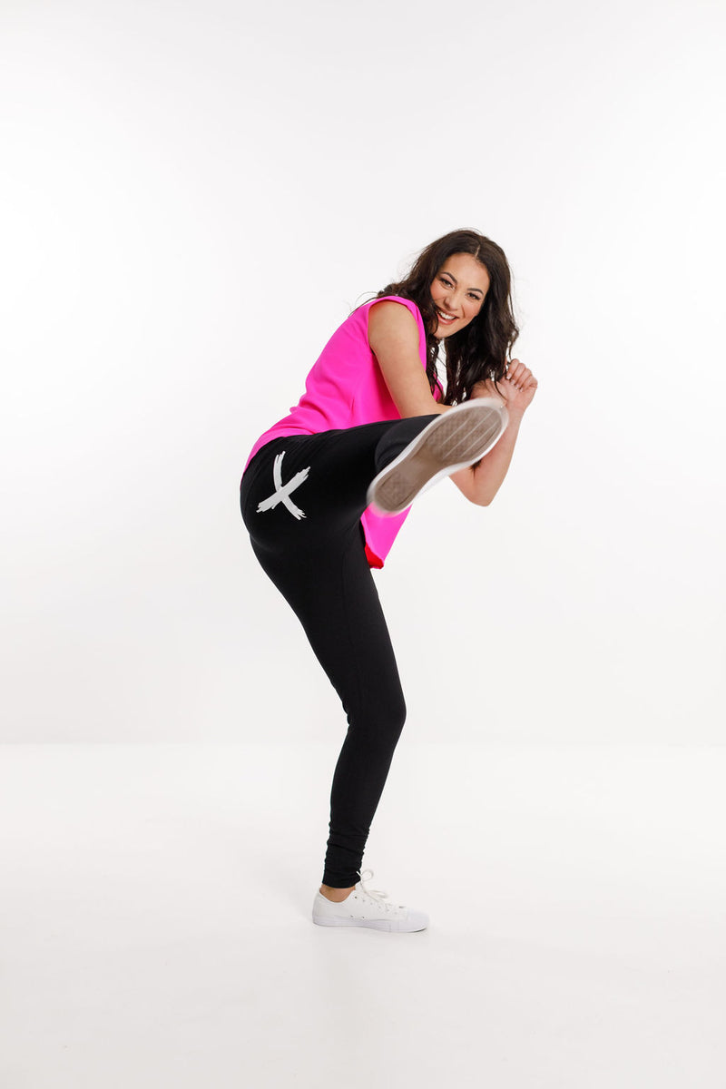 Woman Wearing Home Lee Apartment Pants and a pink top doing a kick 